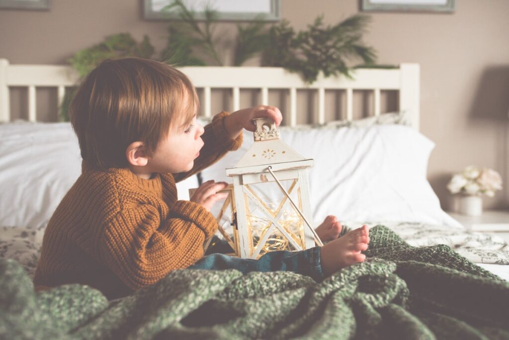 Enfant assis sur son lit avec une lanterne lumineuse dans une chambre a la lumiere douce